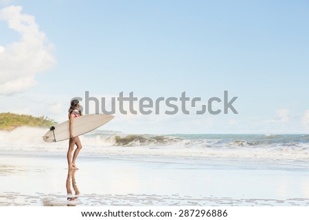 beautiful young woman with long hair in pink swimsuit with surfboard wait on surf spot at sea beach