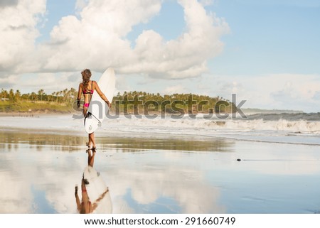 beautiful girl with long hair in a pink swimsuit with surfboard walking to surf spot on ocean beach
