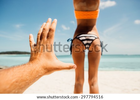 Mans hand trying to touch tanned fit ass of a sporty young beautiful woman in a sexy stripped bikini on a ocean shore background. Outdoor lifestyle picture on a hot sunny summer day.