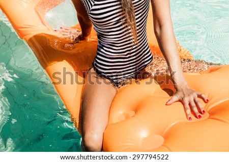 Sporty young beautiful lady in a striped black and white swimsuit sits astride on an inflatable mattress in the refreshing pool. Outdoor lifestyle picture on a hot sunny summer day.