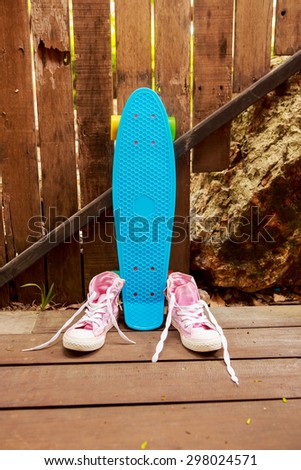 Pink converse sneakers with untied laces on a wooden floor near blue penny skate board longboard with multi color wheels. Urban hipster outfit