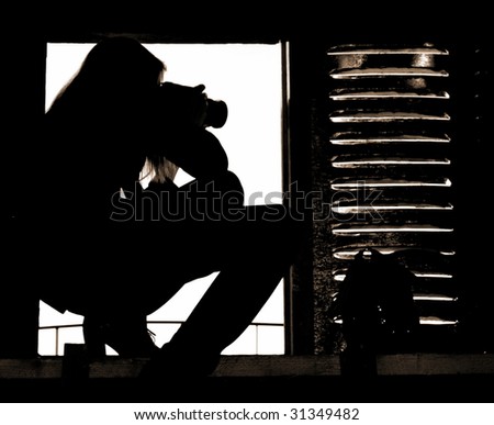 Silhouette of the professional girl-photographer taking pictures from attic window