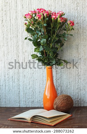 Still life: roses in orange vase, vintage book and coconut.