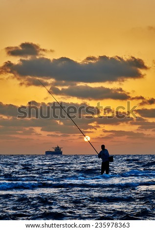 Man fishing in the sea surf at sunset