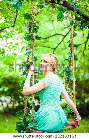 beautiful girl in a green dress on a swing in the summer garden. rear view