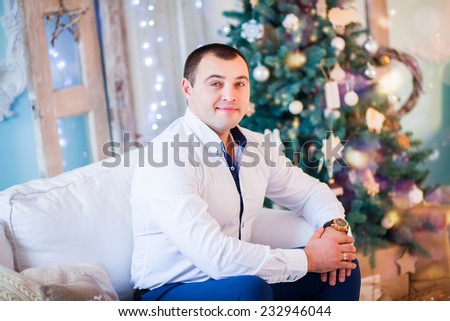 Young man sitting on couch  alone, in front of christmas tree on living room