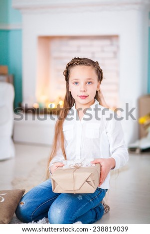 little girl sitting by the fireplace and holding a gift
