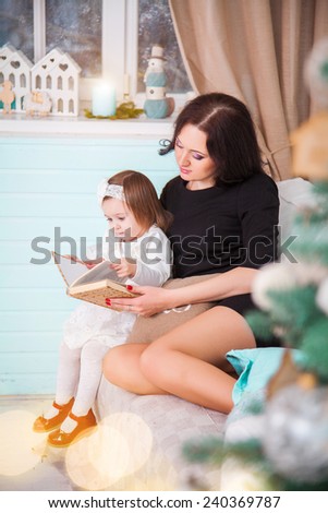 Portrait of happy young mother with child reading book on Christmas evening.