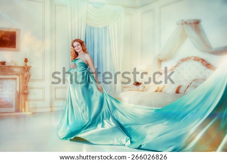 Beautiful young pregnant woman with blue  silk material in bedroom. Happy blonde pregnant girl with blowing blue material.