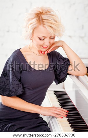 Portrait of beautiful woman in  black dress sitting at the white piano