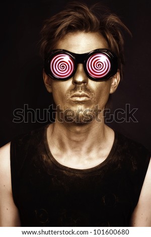 Portrait of young actor with bronze theatrical makeup and in the strange glasses on black background