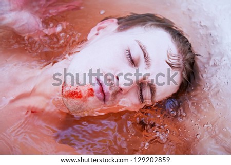 Dead man\'s face with a bloody wound in water closeup