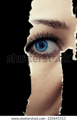One eye of a young woman spying through a hole in the wall
