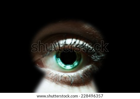 Womans eye peeking through a keyhole concept for curiosity, stalker, surveillance and security