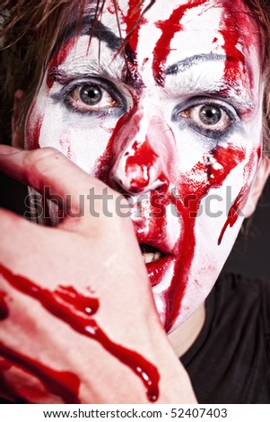 Portrait of mime with blood on face and hand on black background close up
