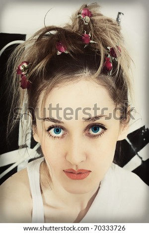 Blue-eyed face of a beautiful young woman with roses woven into the hair