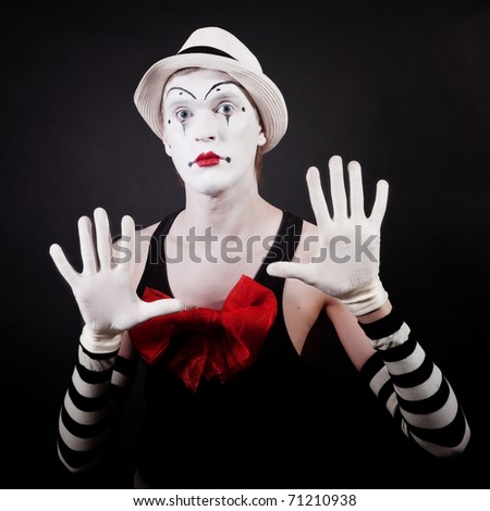 Portrait of a theater actor in makeup funny mime with a red bow on the chest in white hat and striped gloves on a black background