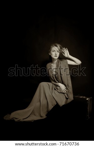 Retro portrait of beautiful young woman in long dress, sitting on old suitcase
