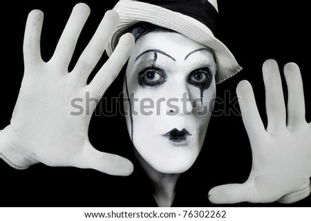 face and hands of mime with dark make-up on black background