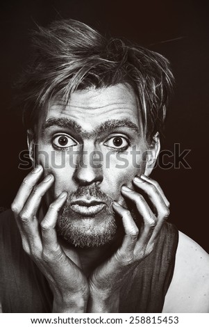 Monochrome portrait of young attractive man with a silvery makeup on her face and hands against a black background