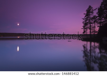 Moonlight over a Swedish lake, the trees and moon are reflecting in the water