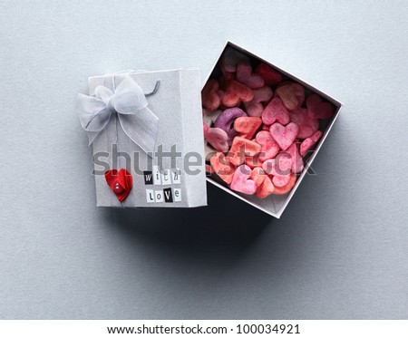 Open gift box with lots of cute little hearts inside. On gray textured paper background.