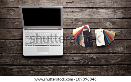 White laptop with designer color swatches on old wooden table.