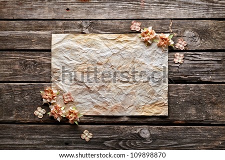 Old crumpled paper with dried flowers or craft flowers on old wood. Sweet holiday background.
