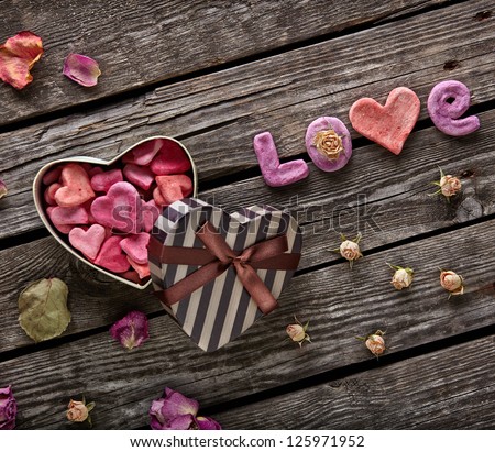 Word Love with Heart shaped Valentines Day gift box on old vintage wooden plates. Sweet holiday background with rose petals and small hearts.