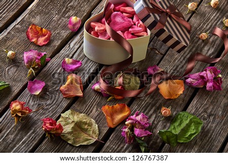 Abstract holiday background with open heart shaped Valentines Day gift box on old vintage wooden plates. With rose petals, small hearts, curved ribbon.