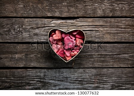 Open heart shaped Valentines Day gift box with heap of small hearts inside on old wooden background.