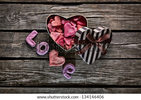 Open heart shaped Valentines Day gift box with heap of small hearts inside and word love on old wooden background.
