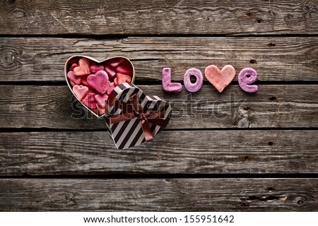 Open heart shaped Valentines Day gift box with heap of small hearts inside and word love on old wooden background.