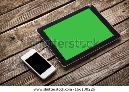 Digital tablet computer and white smart phone with isolated screens on old wooden desk.