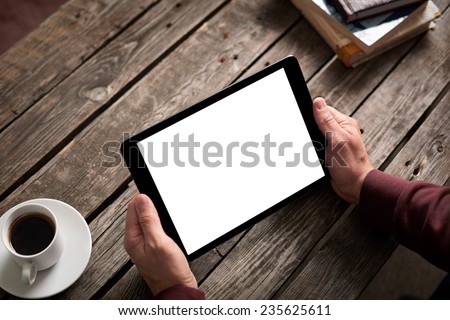 Digital tablet computer with isolated screen in male hands over cafe background - table, smart phone, cup of coffee...