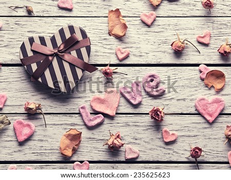 Word Love with heart shaped gift box on old white wooden plates. Sweet holiday background with petals and dried flowers.