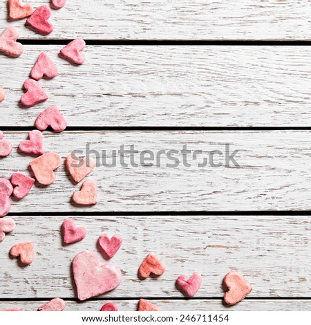 Holiday background with heap of small hearts on white wood table.