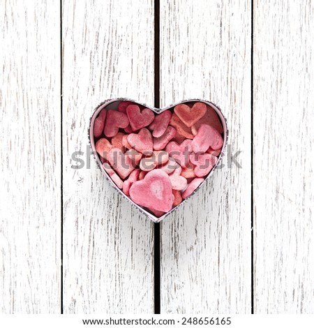 Open heart shaped Valentines Day gift box with heap of small hearts inside on old wooden background.