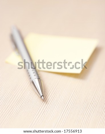 Ball pen lies on the yellow note paper. On the wooden table. Closeup