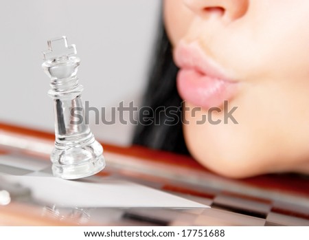 The woman blows off a chess figure from a chessboard. The fallen king. Closeup.