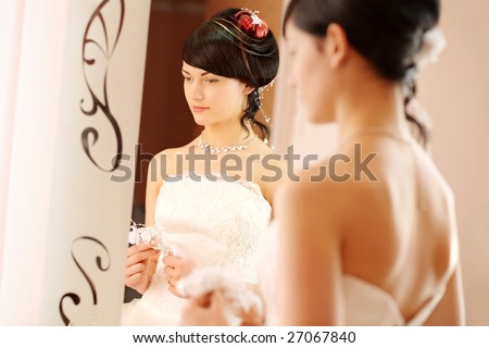 Slim beautiful woman with good hair dress, wearing luxurious wedding dress standing opposite to a mirror.