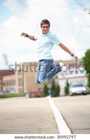 Shot of a young man, that is jumping at the city street. He is happy. He is smiling.