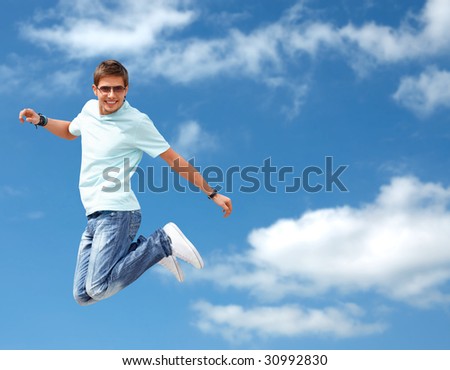 Shot of a young man, that is jumping on the sky background. He is happy. He is smiling.