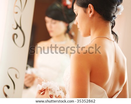 Closeup wedding shot of a slim beautiful woman wearing luxurious wedding dress standing opposite to a mirror.