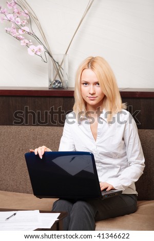 Businesswoman sitting on the sofa in cozy interior with laptop and documents. Looking in camera.
