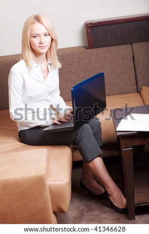 Businesswoman sitting on the sofa in cozy interior with laptop and documents. She is smiling.