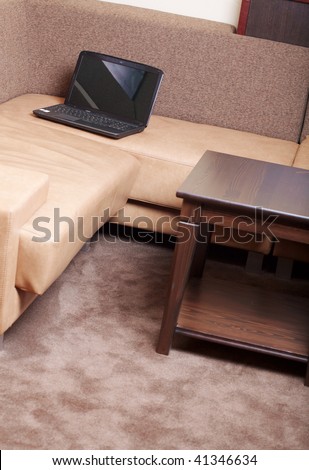 Notebook (laptop) on a leather sofa in cozy interior. There is a table near it.