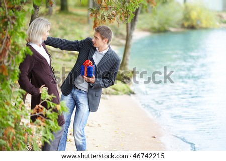 Young happy couple having fun at beach. Boyfriend wants to give gift-box to girlfriend.