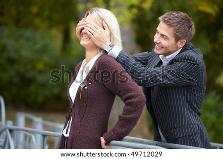 Young happy couple having fun at the park. Man puts his hands over girl\'s eyes.