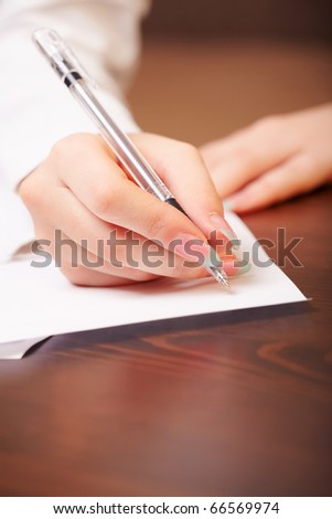 Woman hand writing on paper by ball pen. Closeup shot on wooden table.